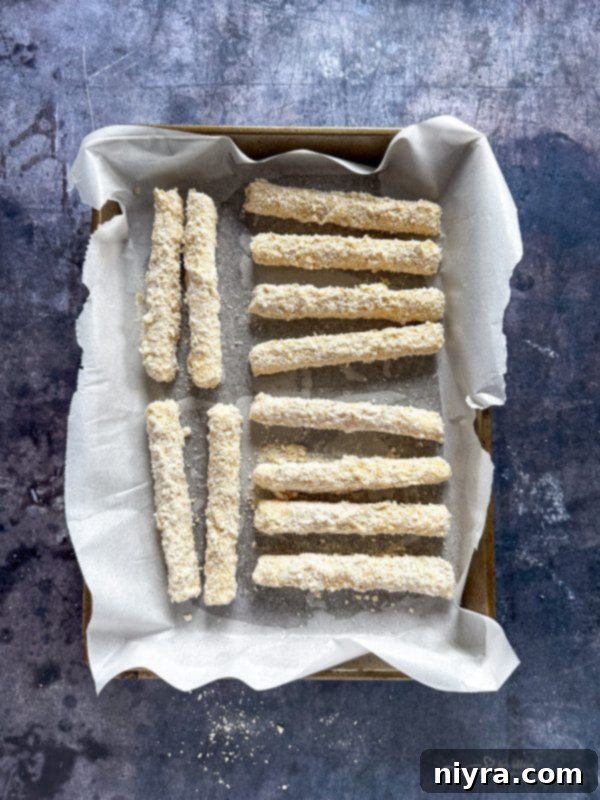 A hand dipping a mozzarella stick into the breadcrumb mixture, ensuring a complete coating.