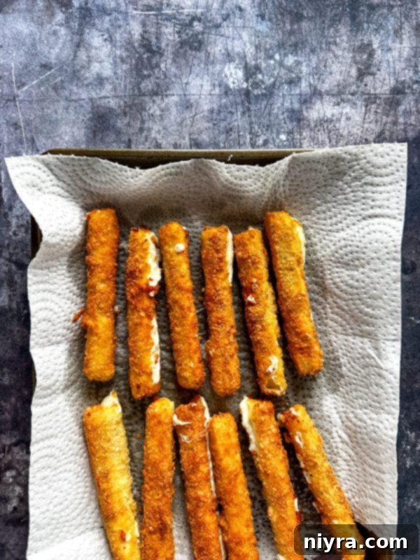 Mozzarella sticks sizzling in hot oil in a skillet, turning golden brown as they fry.