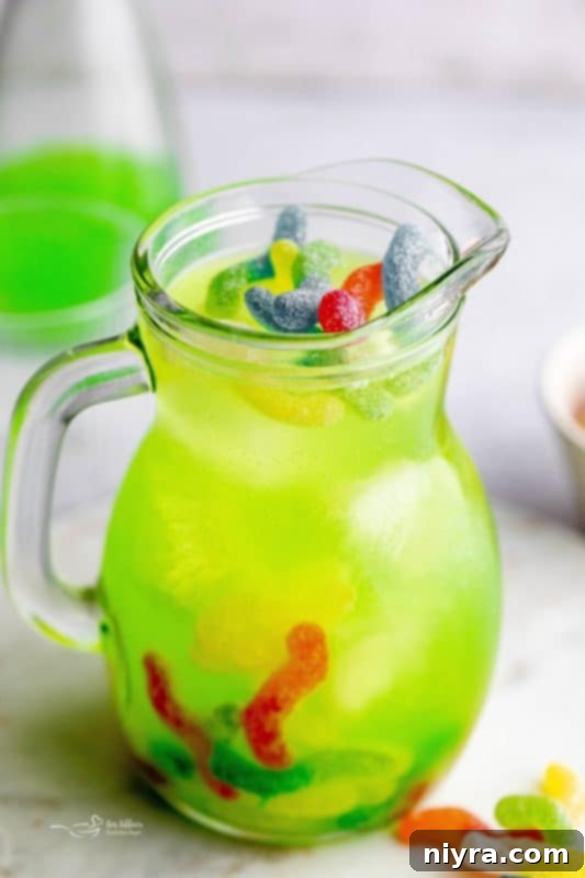 Halloween Kids Punch - a pitcher filled with green punch, garnished with sour worms and ice, ready to serve.