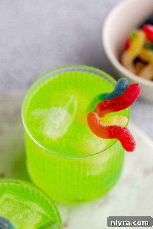 A pitcher of Halloween Kids Punch with a glass next to it, showing floating sour worms and ice.