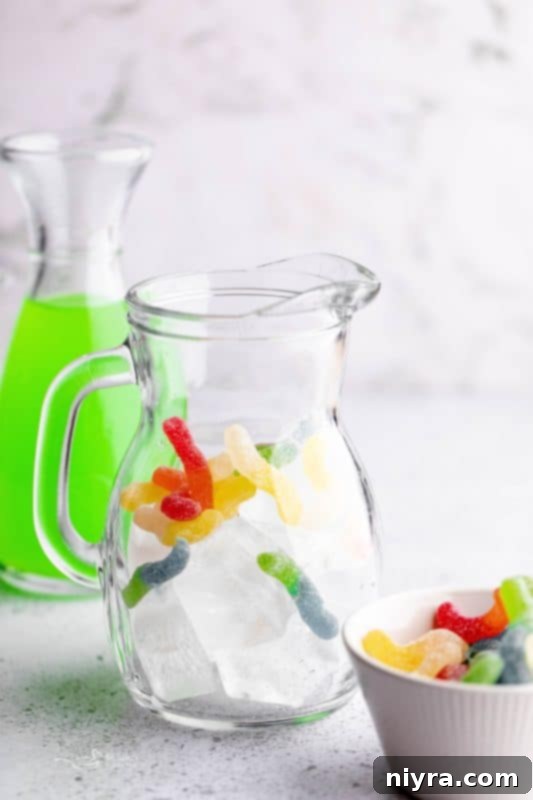 Step 2: Adding a handful of sour worms to a pitcher with ice for Halloween Kids Punch.