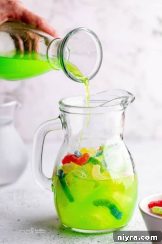 Step 3: Pouring green Gatorade into a pitcher with ice and sour worms for Halloween Kids Punch.