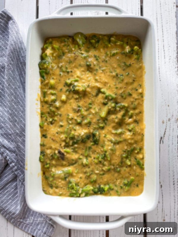 Top view of uncooked broccoli and cheese casserole in white baking dish