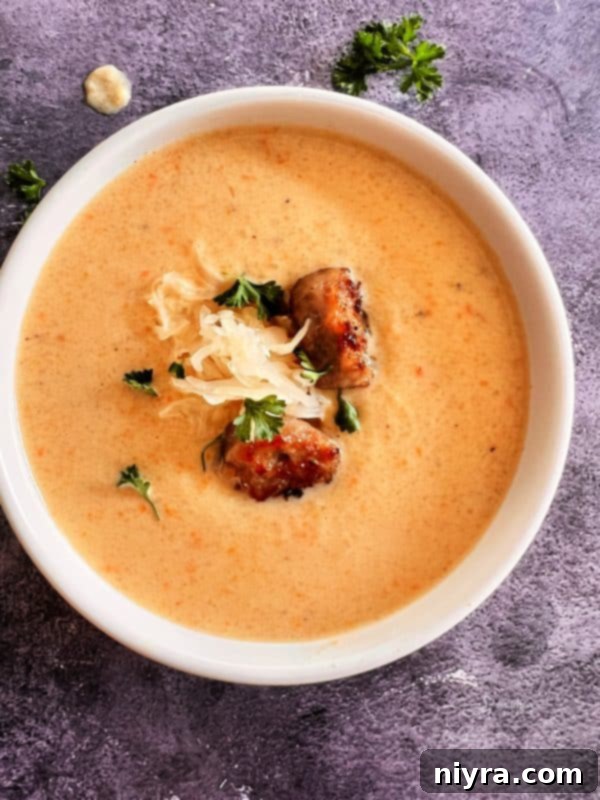 A bowl of creamy French Sauerkraut Soup with sliced bratwurst and fresh parsley on top.