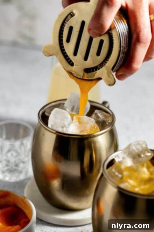 Straining the cocktail mixture into a copper mug filled with ice.