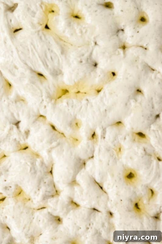 Baker gently poking focaccia dough with fingers to create characteristic dimples