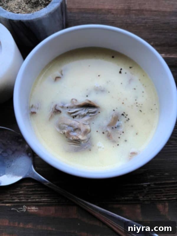 Oyster stew in a white bowl with a spoon, ready to be served.
