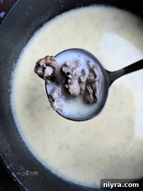 Close-up of creamy oyster stew in a white bowl with a spoon.