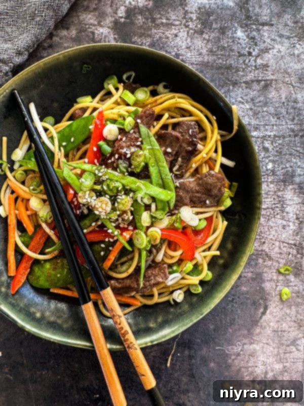 Close up of Chops sticks atop the Beef Lo Mein in a dark green bowl.