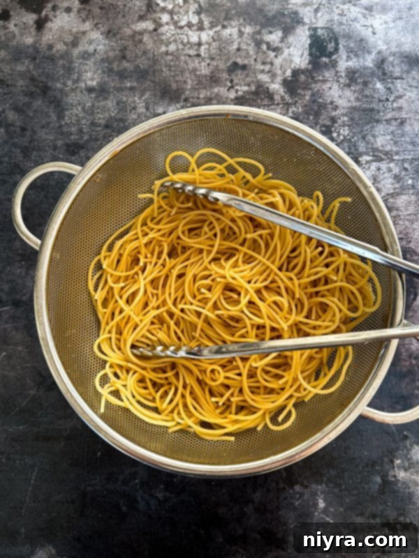 A bowl of uncooked noodles next to a cutting board with chopped vegetables.