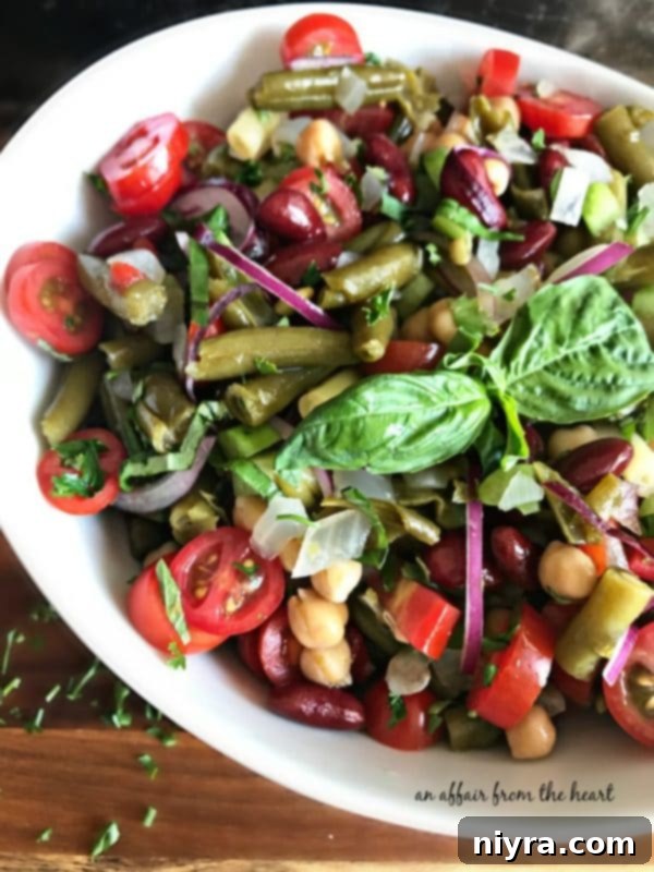 Close-up of a colorful Italian Bean Salad in a white bowl, garnished with fresh herbs.