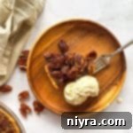 Close up of Slice of pecan pie, a fork and vanilla ice cream on a wooden plate