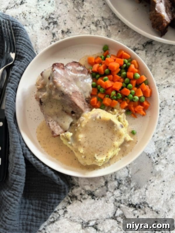 Platter of sliced roasted pork roast, drenched in homemade gravy, with mashed potatoes ready to be served.