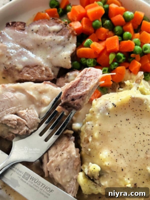A whole roasted pork shoulder served on a wooden board, surrounded by fresh herbs, with a bowl of rich gravy beside it.