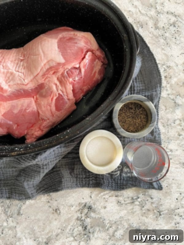 A large cut of raw pork shoulder roast, seasoned and ready for the oven, sitting in a roasting pan.