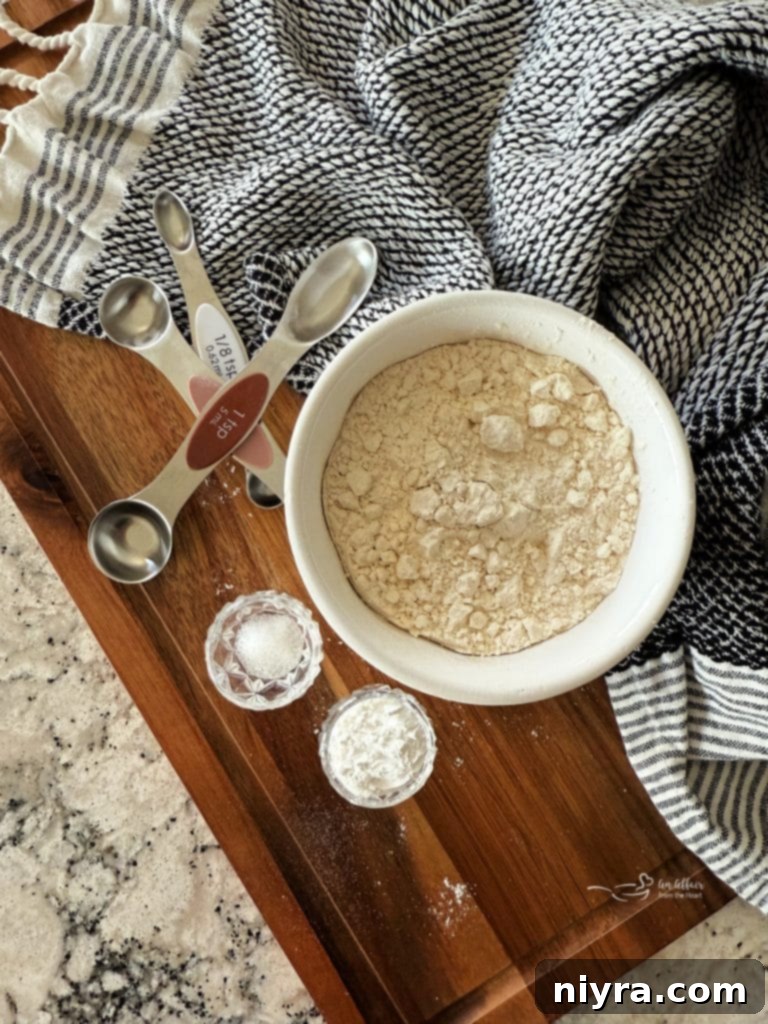 A measuring cup filled with all-purpose flour, a small bowl of baking powder, and a small bowl of salt on a wooden surface.