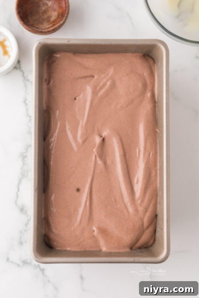 Chocolate malt ice cream mixture being poured into a loaf pan.