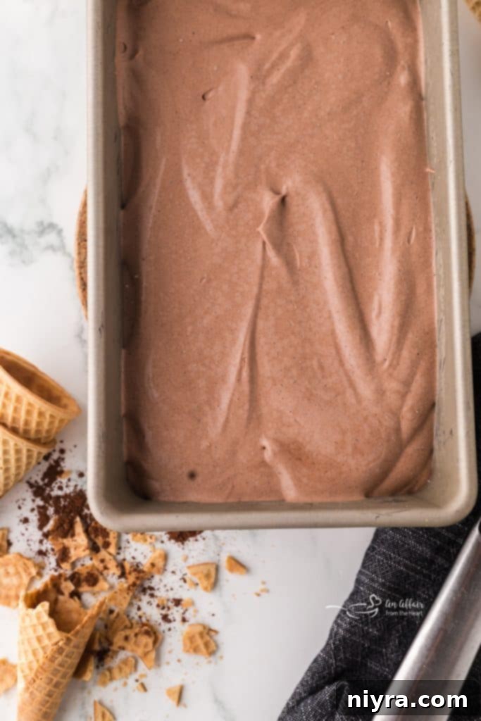 Chocolate malt ice cream covered with plastic wrap in a loaf pan.
