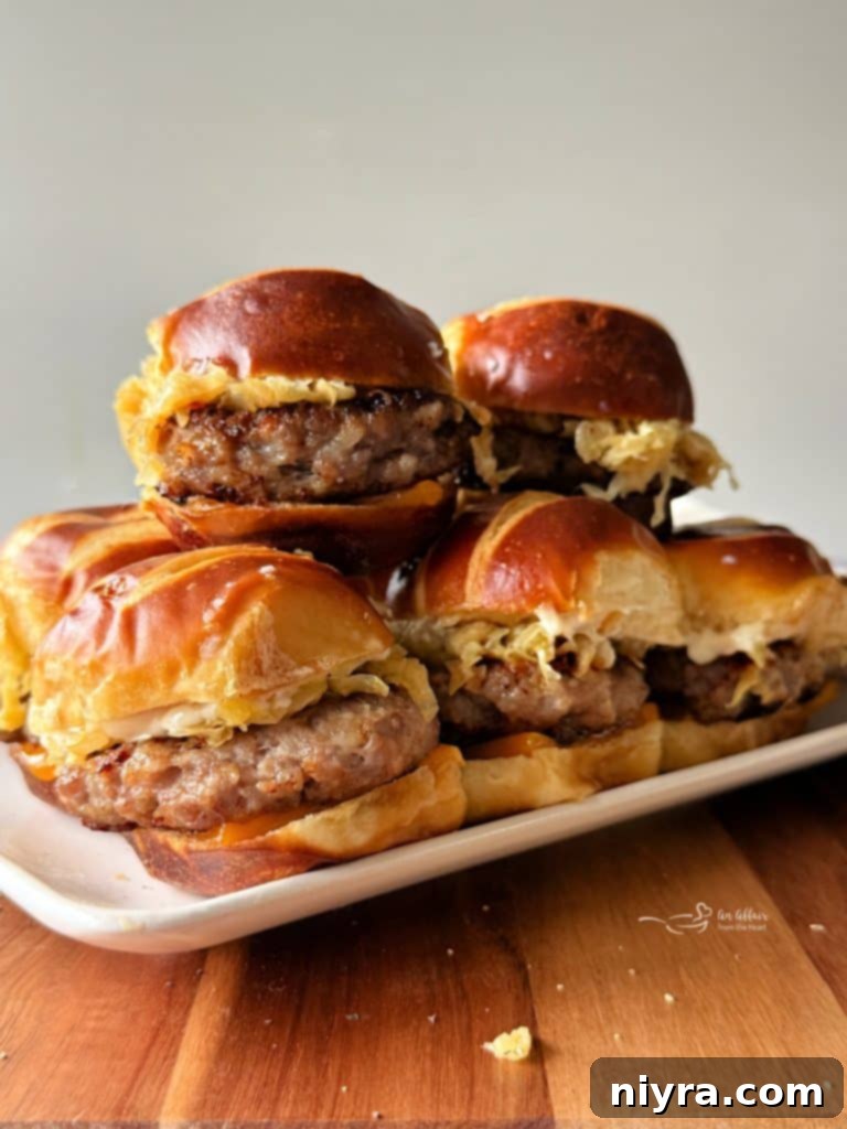 A stack of Bratwurst Sliders with melty cheese and kraut on a white serving platter.