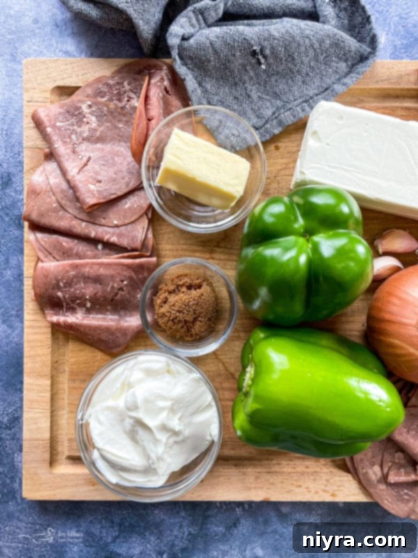 Ingredients for Philly Cheese Steak Dip on a cutting board: roast beef, peppers, cream cheese, provolone, butter, brown sugar, onions, garlic