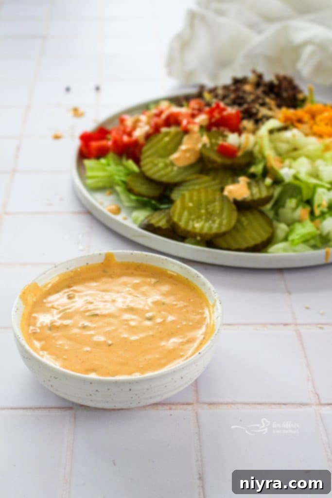 Overhead shot of Big Mac Salad in a white bowl with a spoon, garnished with sesame seeds.