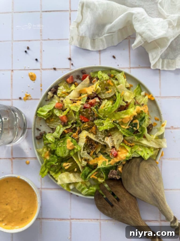 A close-up shot of Big Mac Salad in a white bowl, showing layers of beef, lettuce, cheese, and a generous drizzle of special sauce.
