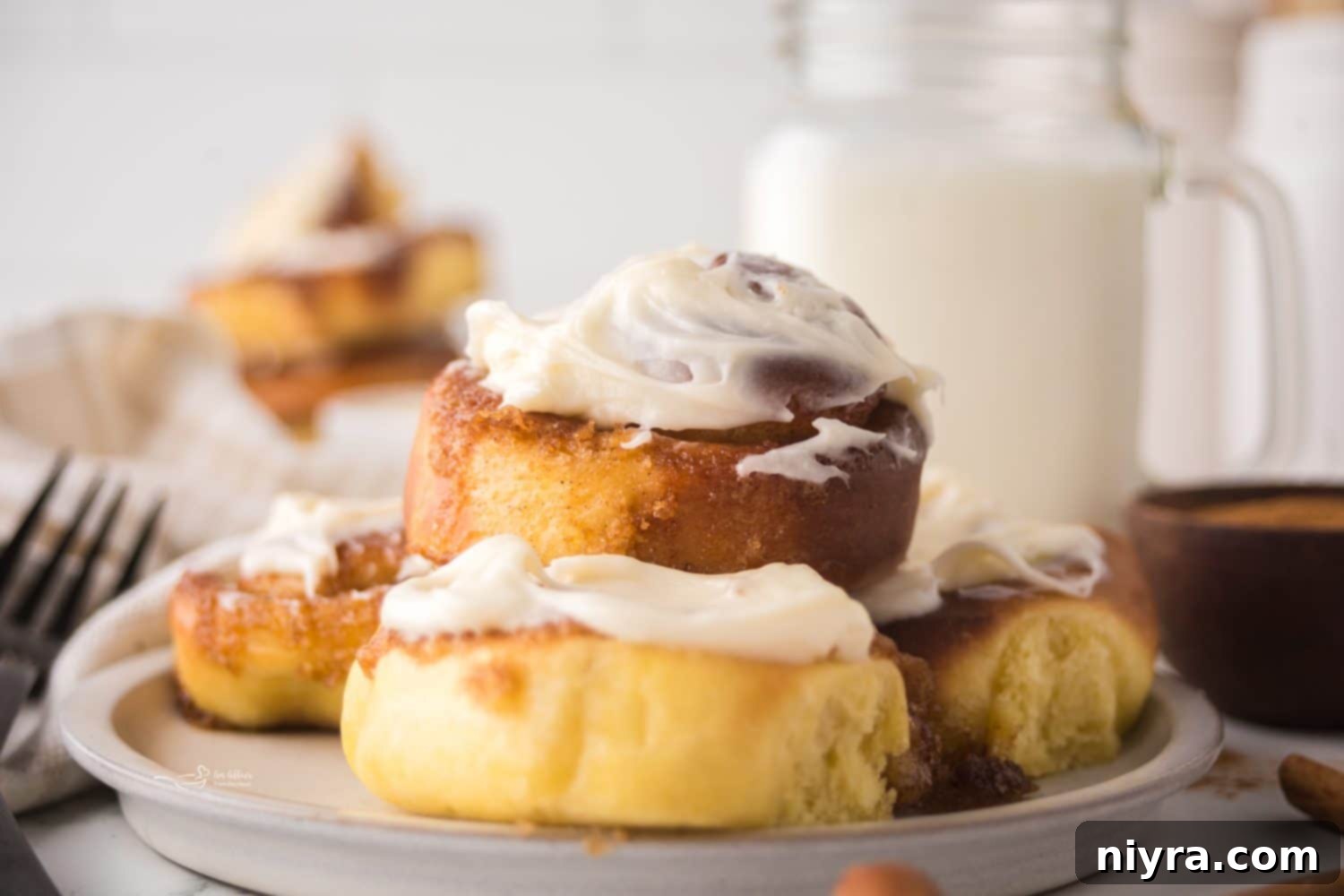 A plate of two freshly baked air fryer cinnamon rolls, drizzled with cream cheese frosting.